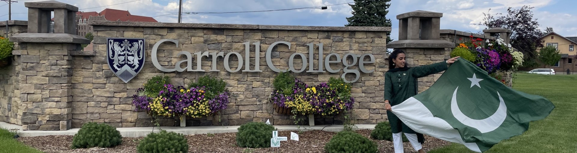 Girl holding a sign in front of a Carroll College sign