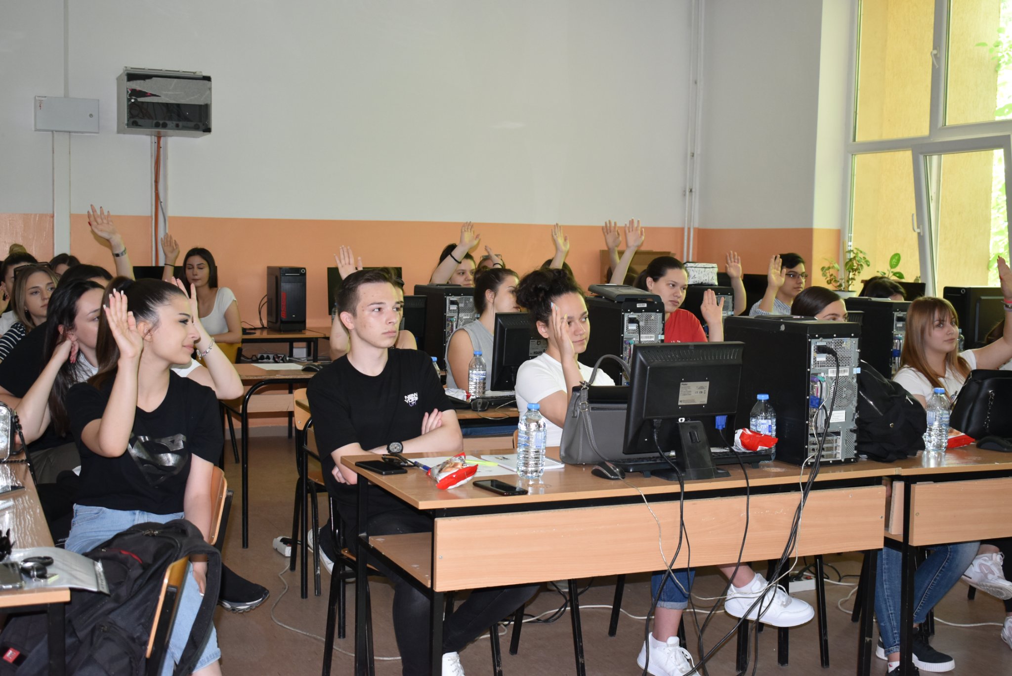 Photo of male and female students in a computer lab, some of them are raising their hands 