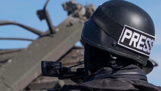 Photo of a journalist in flack vest with a press helmet.