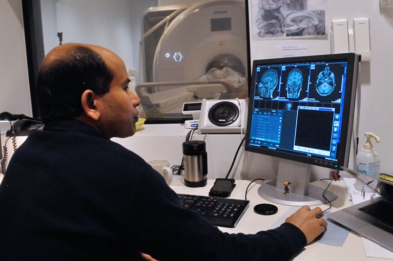 Photo of a researcher looking at brain scans on a computer in front of an MRI machine.