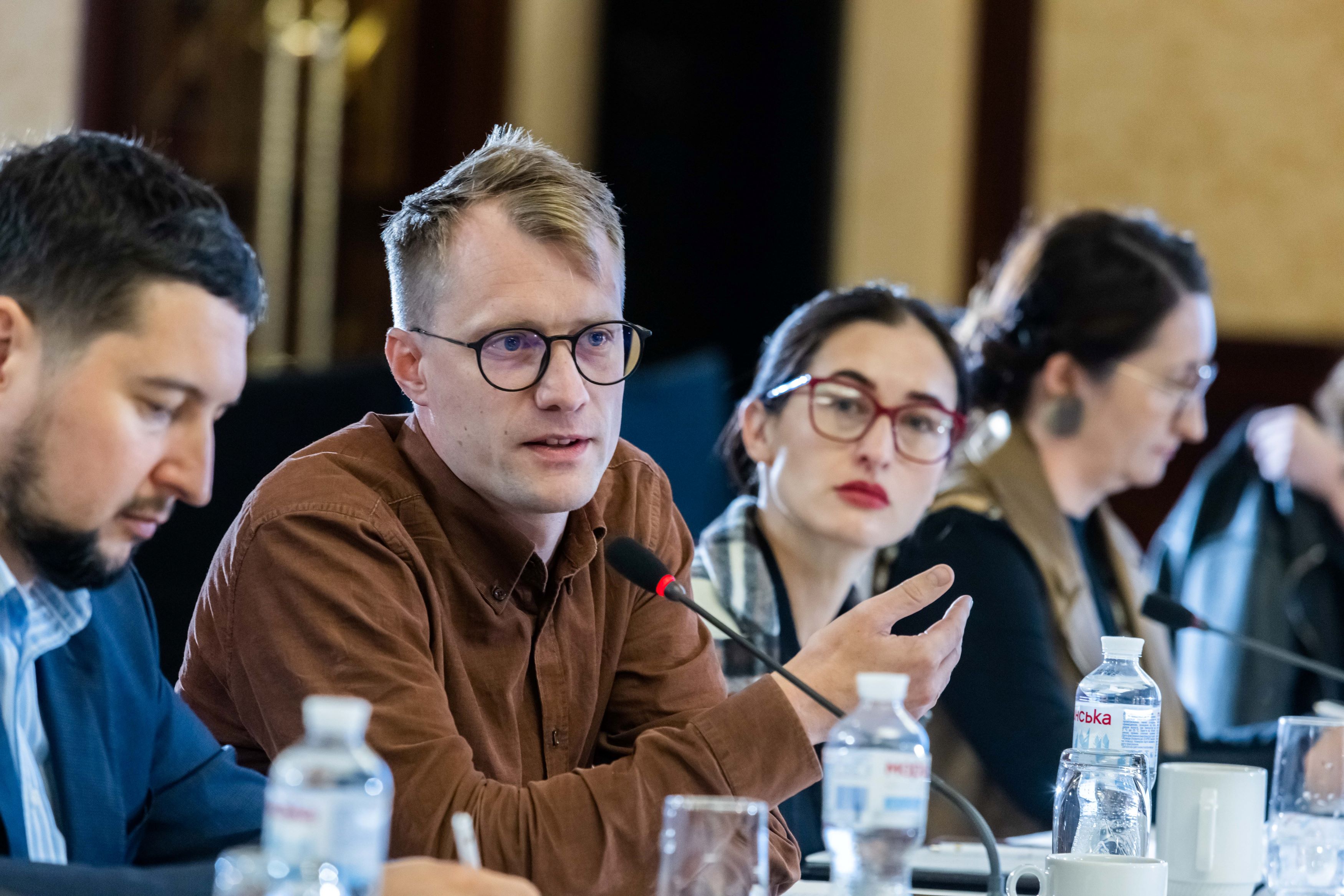 Photo of male and female participants at an event, they are sitting at a table with microphones.